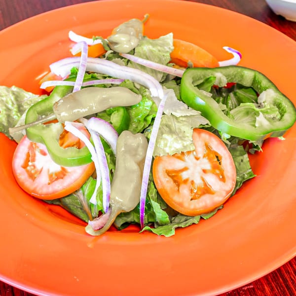 Fresh garden salad with lettuce, tomatoes, green peppers, onions, and banana peppers on an orange plate.