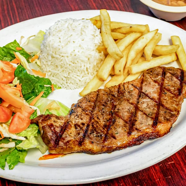 Grilled steak with crisscross marks, a side of white rice, french fries, and a fresh salad.