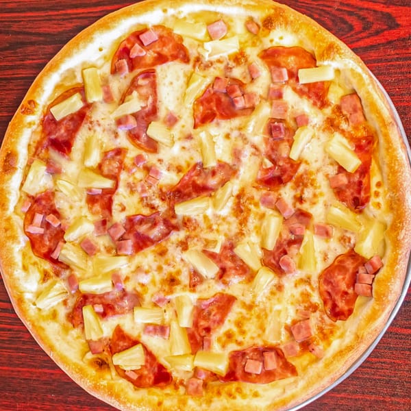 Mr. Pizza Man's Hawaiian pizza, topped with ham, pineapple, and melted cheese on a red wooden table.